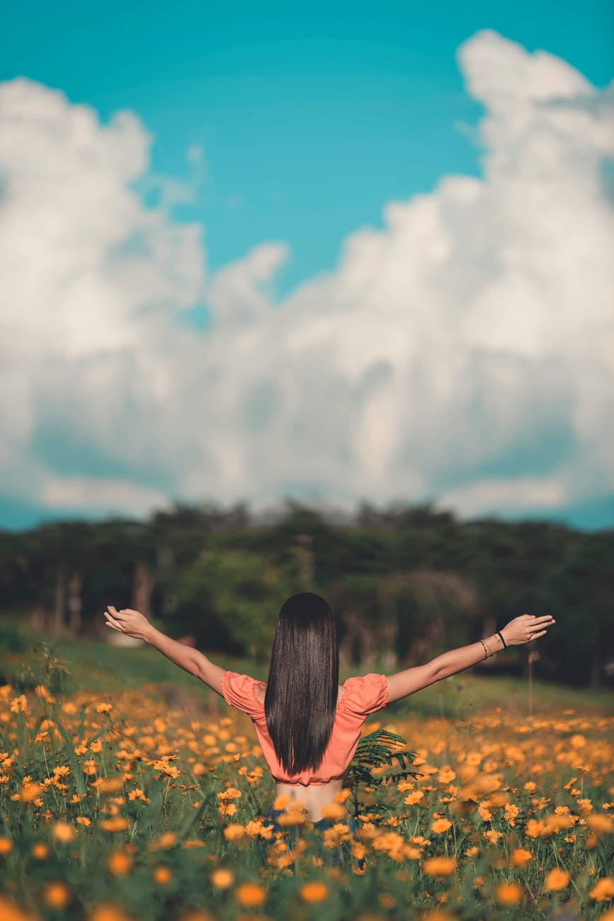 woman standing on flower field and raising her both hands